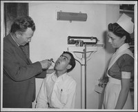 Joseph Sutherland examines a patient while an unknown nurse looks on