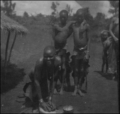 Kisii woman grinding grain while other natives look on