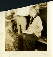 Nellie Druillard sitting on the running board of an automobile, with a man next to her, probably E. A. Sutherland