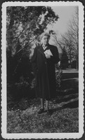 M. Bessie DeGraw in overcoat posing in front of a tree